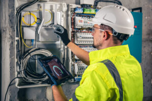 man-electrical-technician-working-switchboard-with-fuses-uses-tablet-scaled.jpg